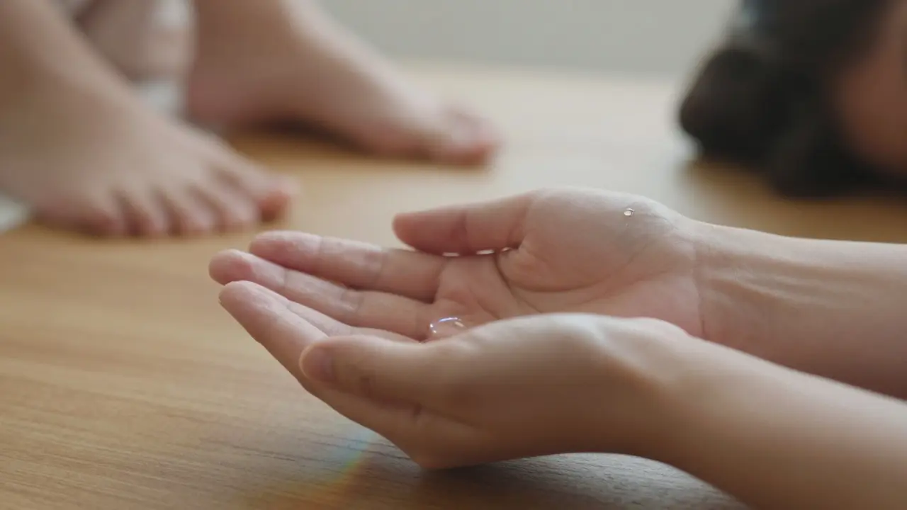 Ruce na dřevěné tabuli s kapkou oleje, symbolizující obnovu a dotek.